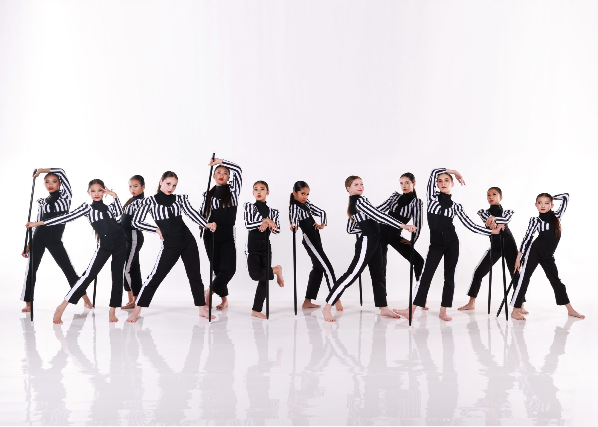 A studio group of young dancers in black and white striped costumes holding canes