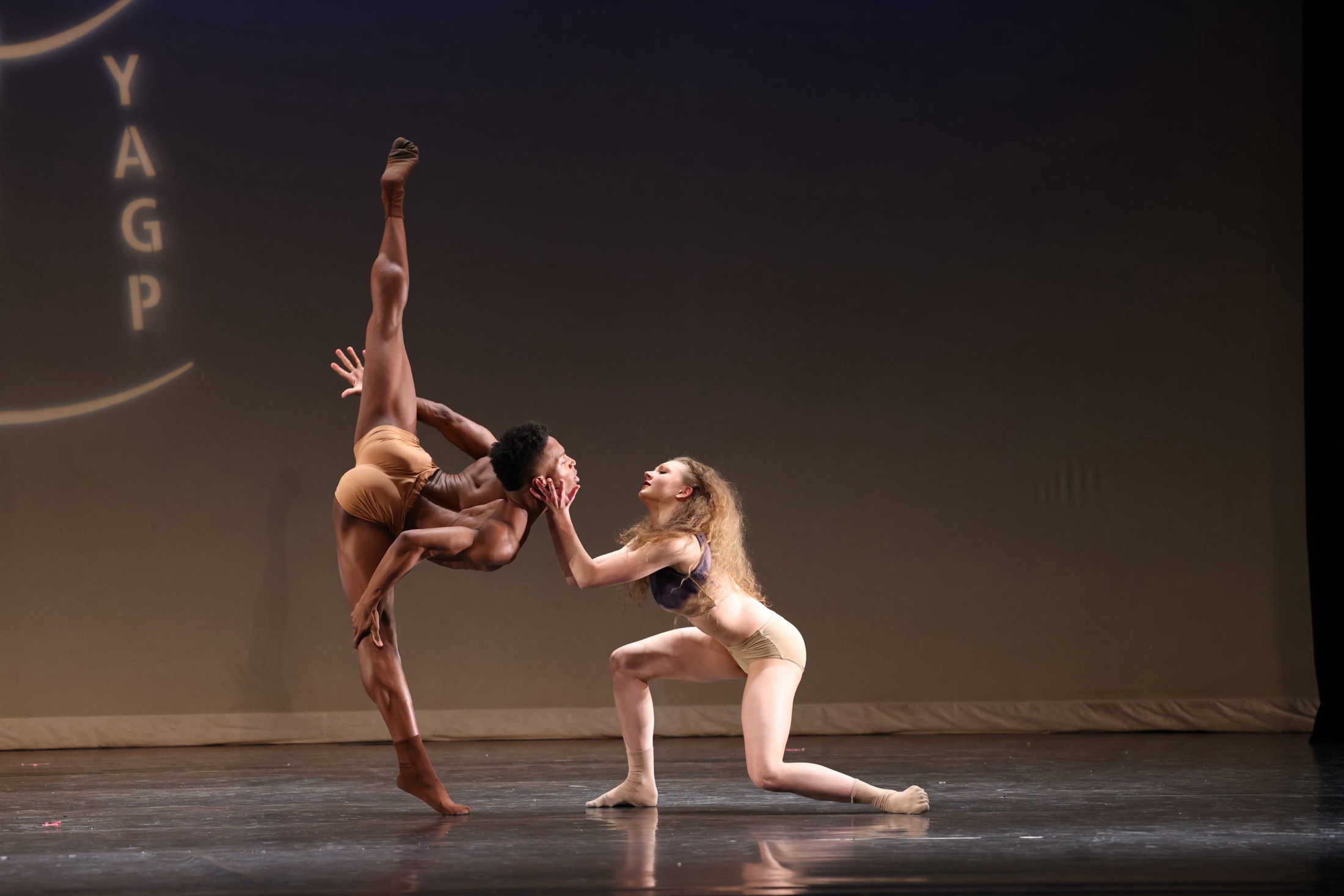 Two dancers in a contemporary duet under warm stage light at Youth America Grand Prix