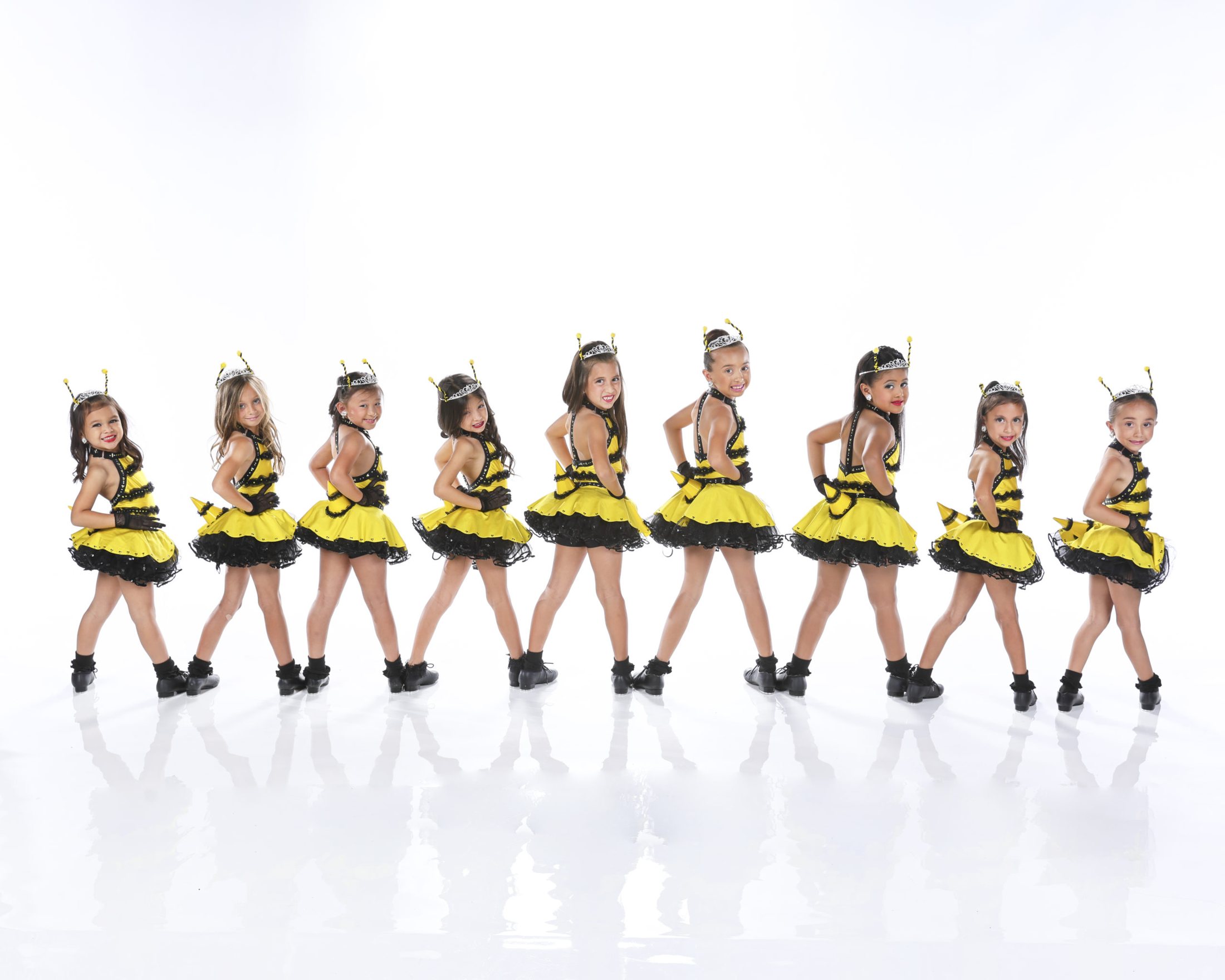 A line of young dancers in yellow and black bee costumes on a white set