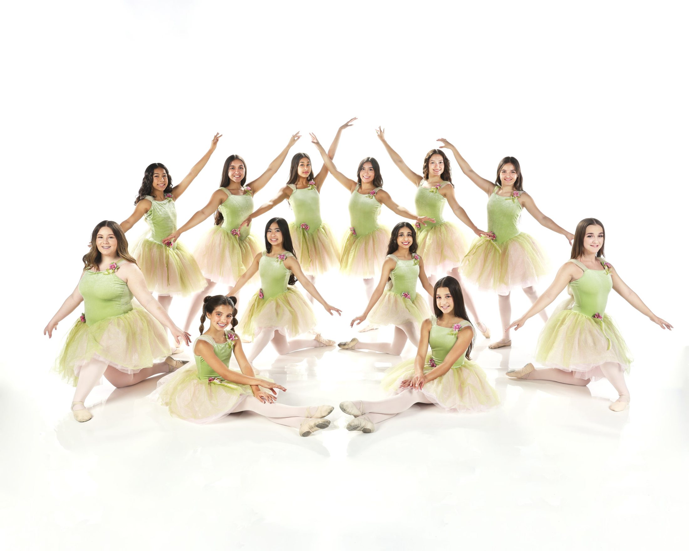 A class of young ballet dancers in pale green tutus posed together on a white set