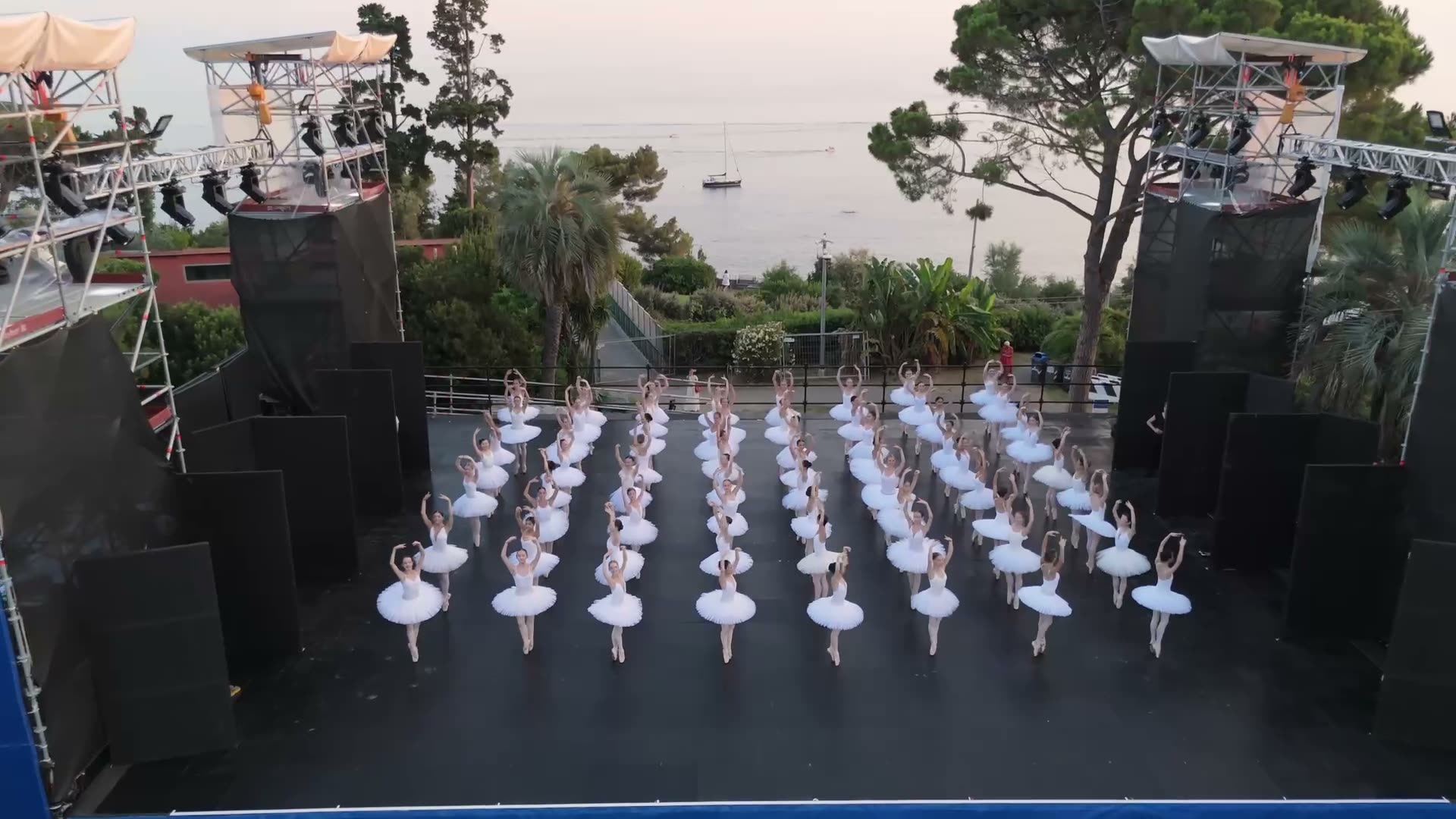 Aerial view of a ballet corps in white tutus on an outdoor stage by the sea