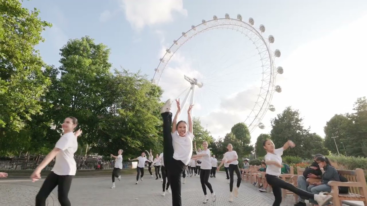 Young dancers performing outdoors in front of a large observation wheel