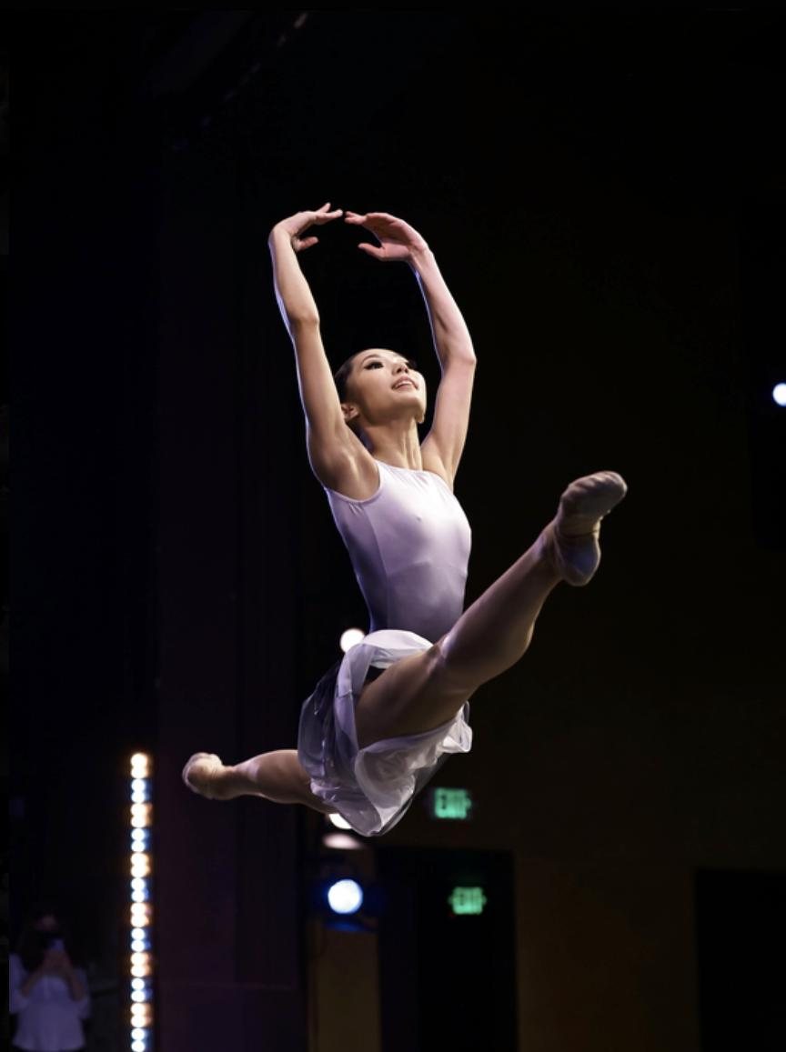 A ballet dancer leaping on a dark competition stage