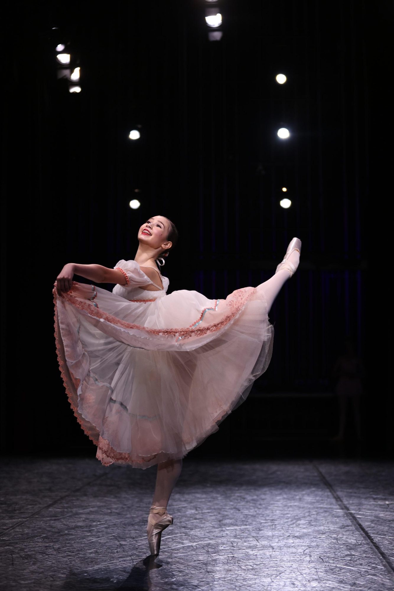 A ballerina in a long romantic tutu in arabesque on a dark stage